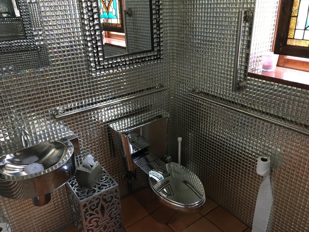 A bathroom with every surfce either metallic or covered in mirror tiles.