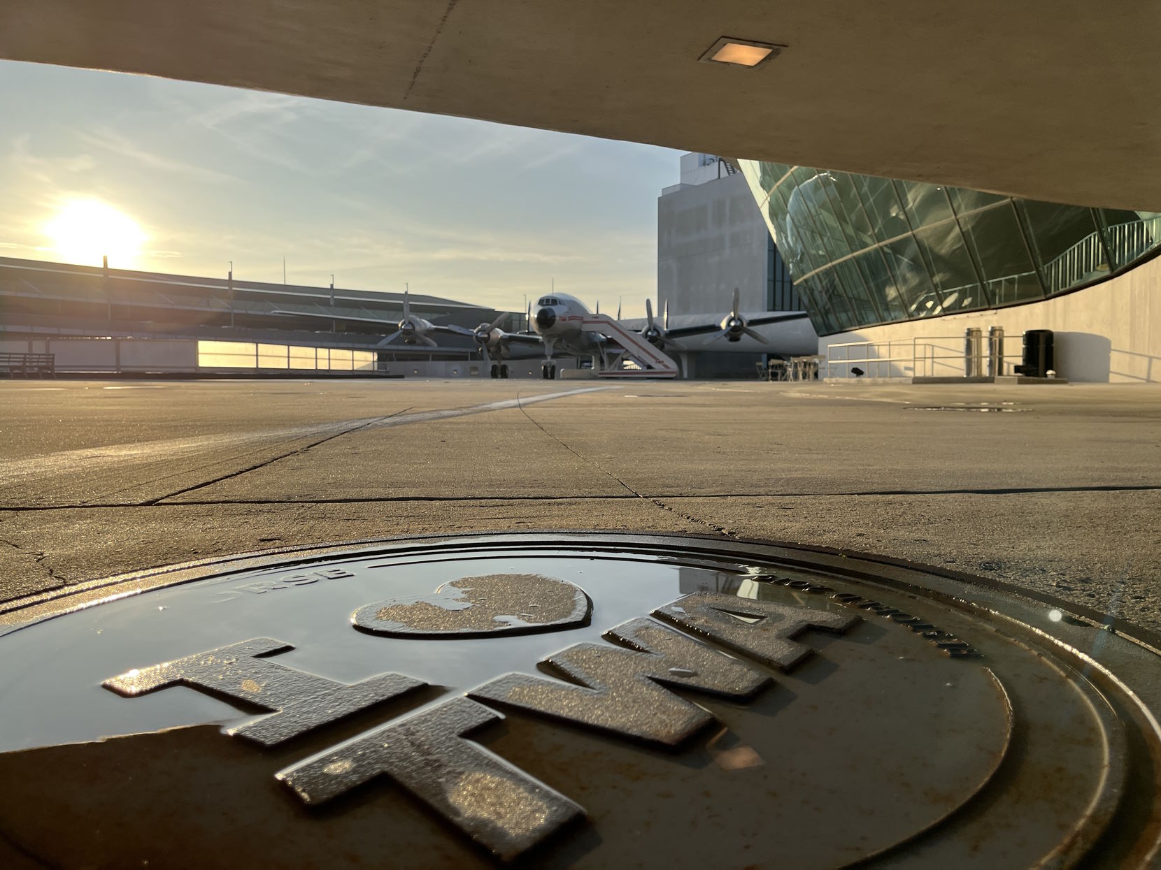 Photo with an 'I heart TWA' manhole in the foreground, and a Lockheed Constellation in the background.
