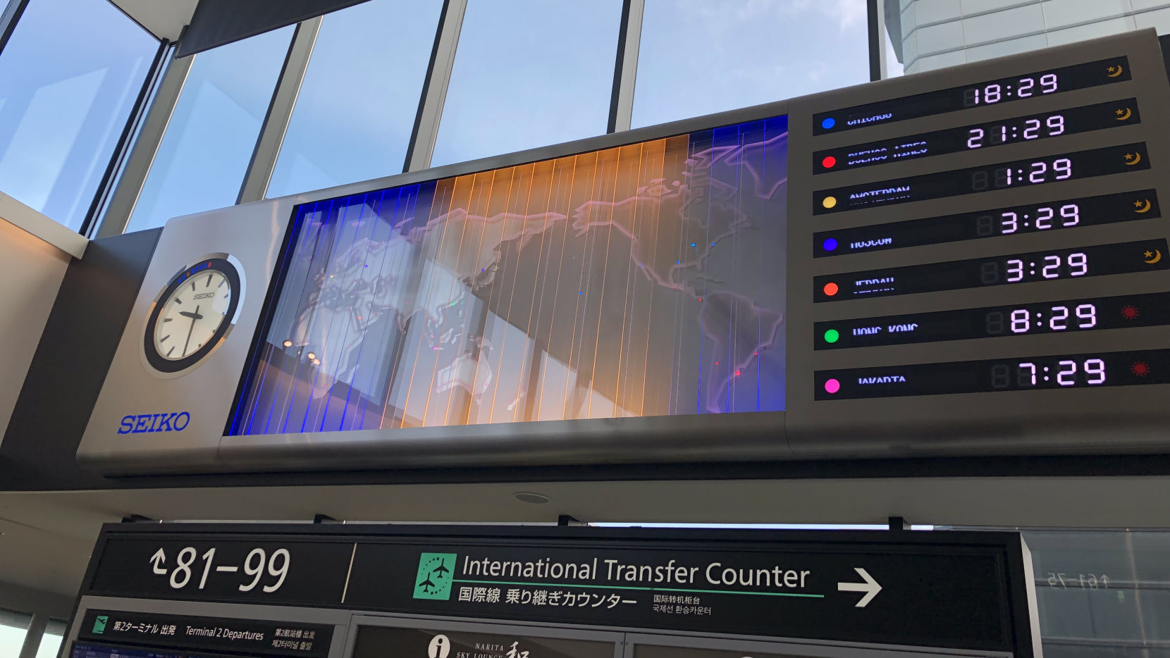 A large board with a clock and a map of the world, with vertical stripes backlit with orange or blue to indicate day or night in that part of the world.