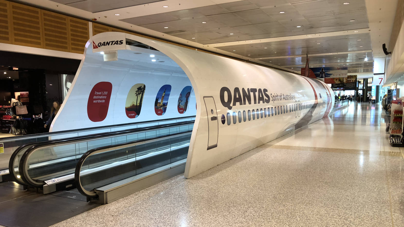 A tunnel enclosing a pair of moving sidewalks shaped to look like the fuselage of a Qantas jet.