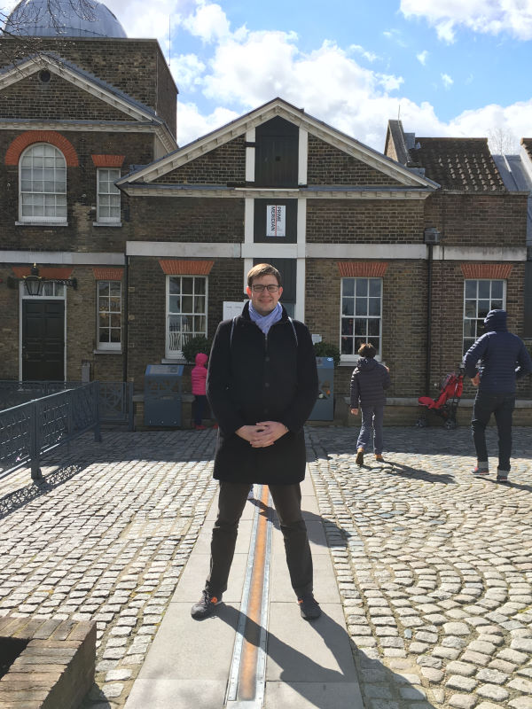 Paul straddling a yellow line labeled Prime Meridian at the Royak Greenwich Observatory.